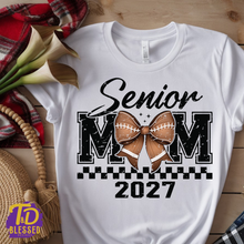 Load image into Gallery viewer, White Senior Mom 2027 football shirt with distressed black lettering, brown football bow, and checkerboard accent